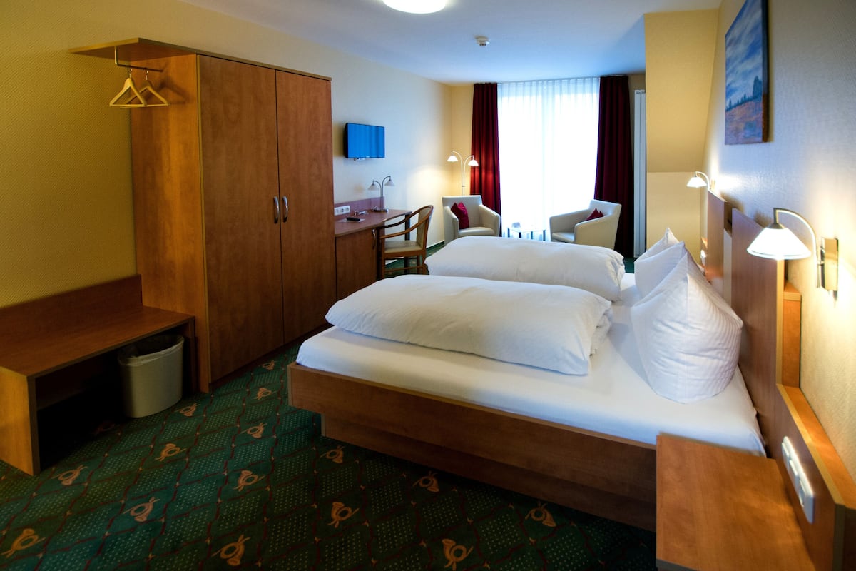 A hotel room with a bed, a desk, a chair, a wardrobe, and a television.
