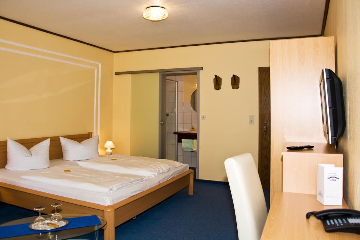 A hotel room with a double bed, a desk with a telephone, a chair, a television, and a small table with a tray of glasses.