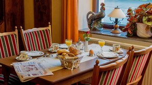 A breakfast table set with plates, cups, a basket of bread, and a newspaper.