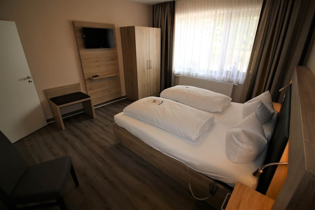 A hotel room with a bed, a TV mounted on the wall, a wardrobe, and a small table.
