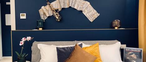 A bedroom with a dark blue wall, a saxophone, and a book titled "Ray Charles: The Ultimate Collection" on a nightstand.