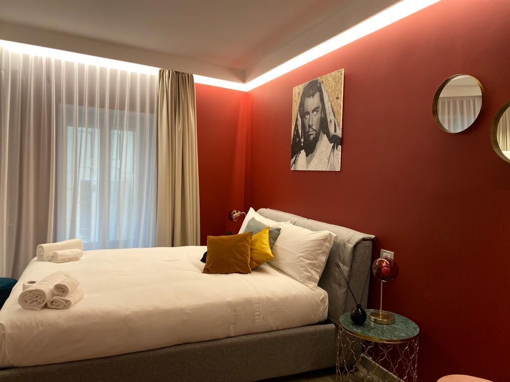 A hotel room with a bed, a round mirror, a painting on the wall, and a window with curtains.