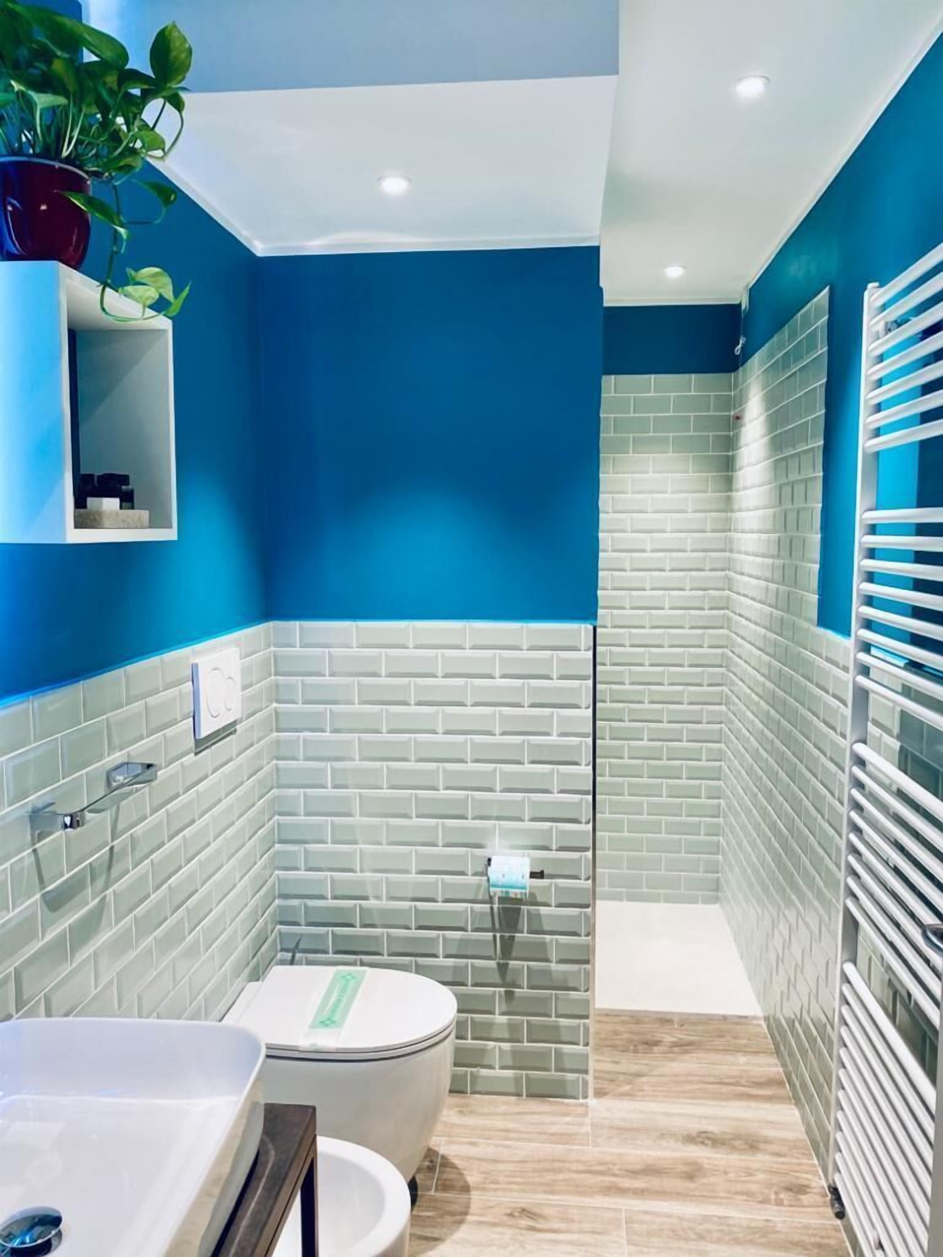 A bathroom with blue walls, a white bathtub, a toilet, and a glass shower enclosure.