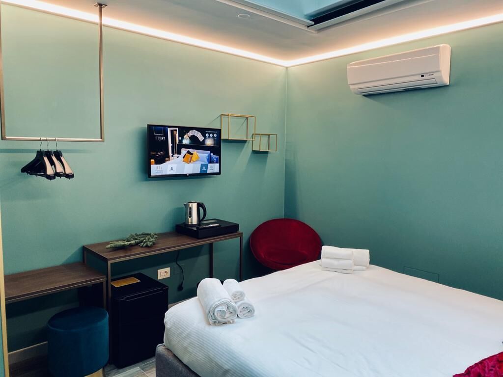 Quarto de hotel com cama, escrivaninha, cadeira, televisão e ar condicionado.