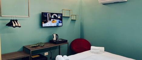 Quarto de hotel com cama, escrivaninha, cadeira, televisão e ar condicionado.