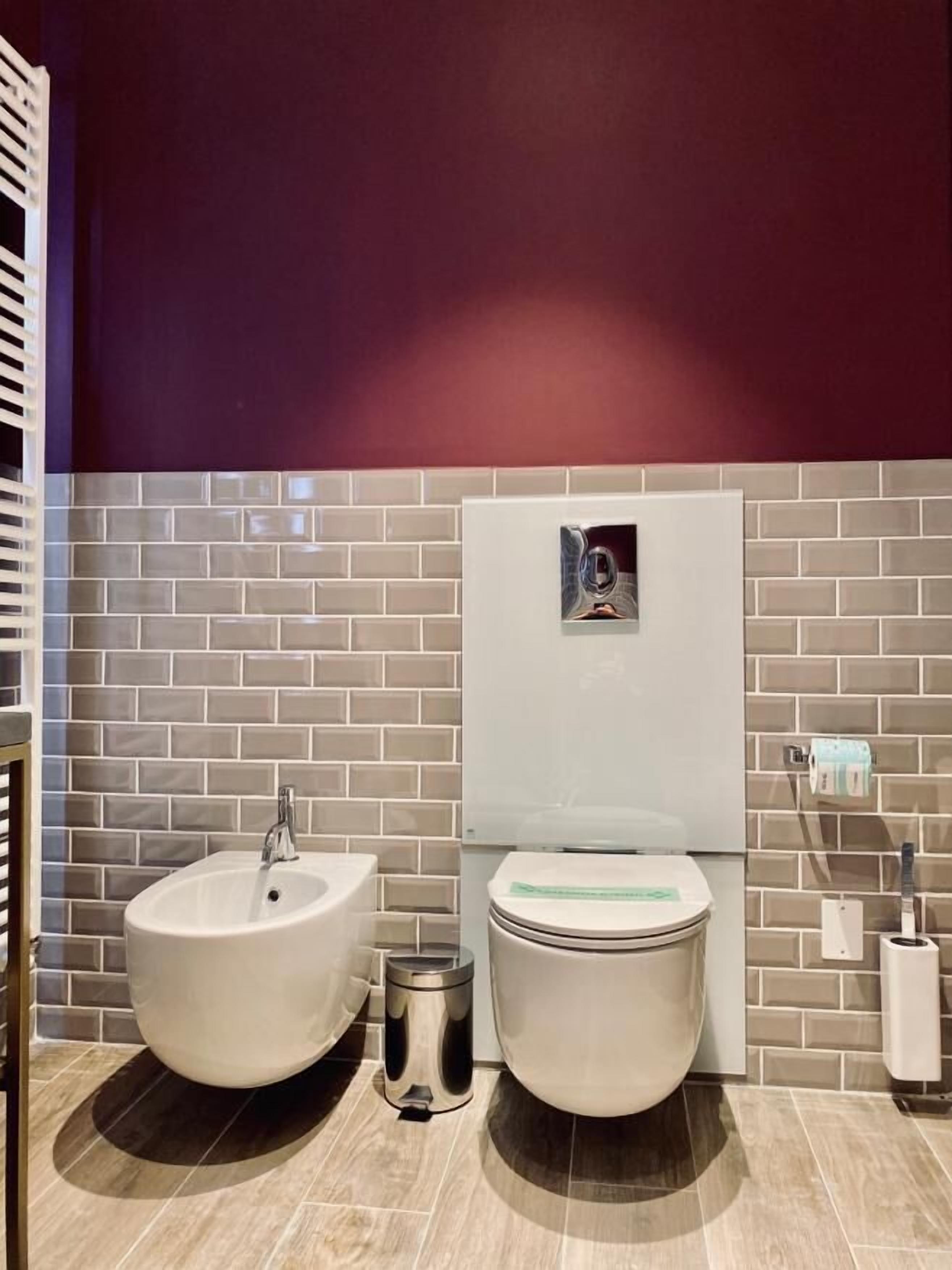 A modern bathroom with two sinks, a toilet, and a trash bin.