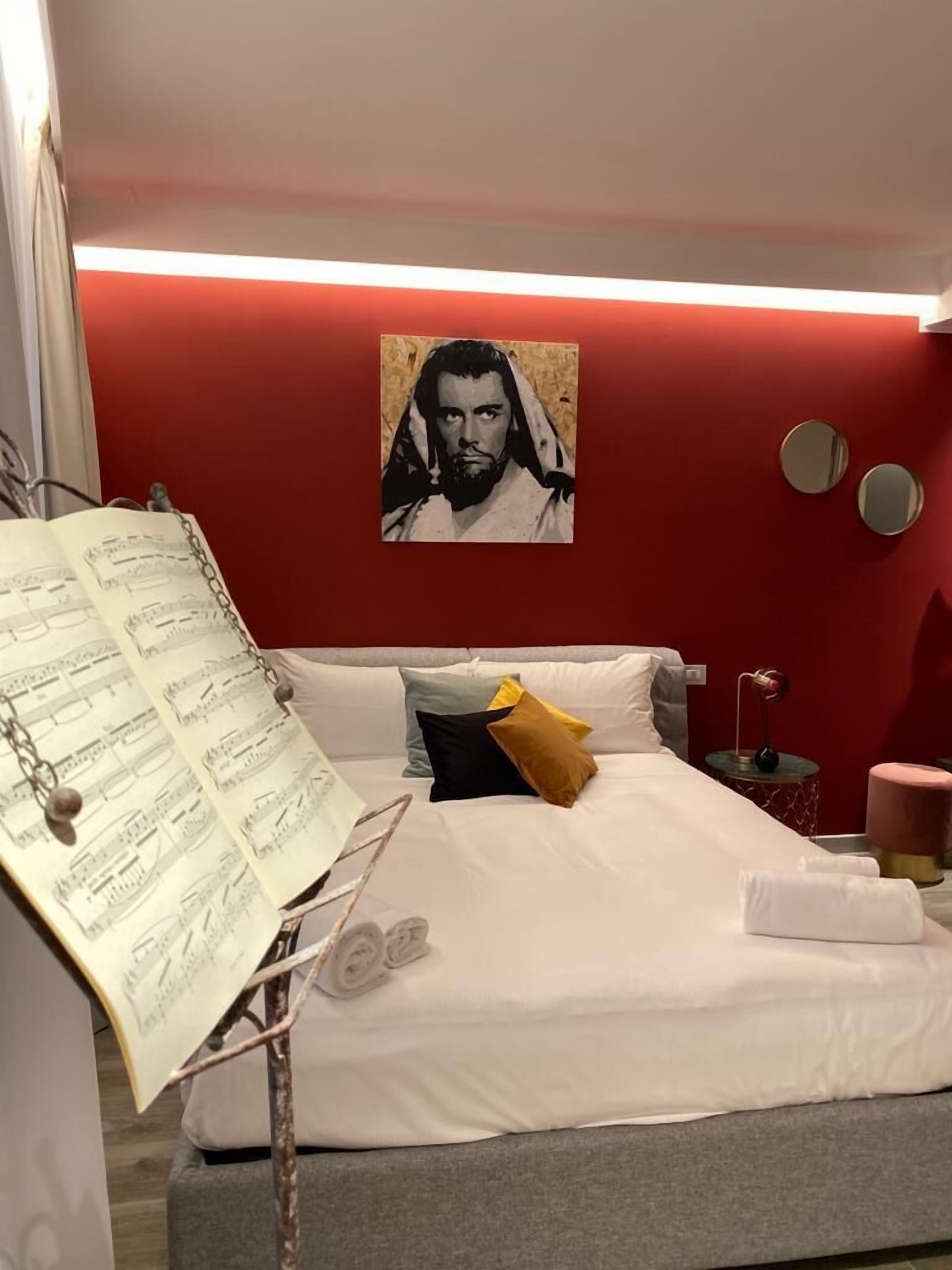 Un dormitorio con cama, almohadas, una mesita de noche, una lámpara y un póster en la pared.