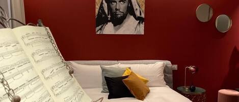 Un dormitorio con cama, almohadas, una mesita de noche, una lámpara y un póster en la pared.