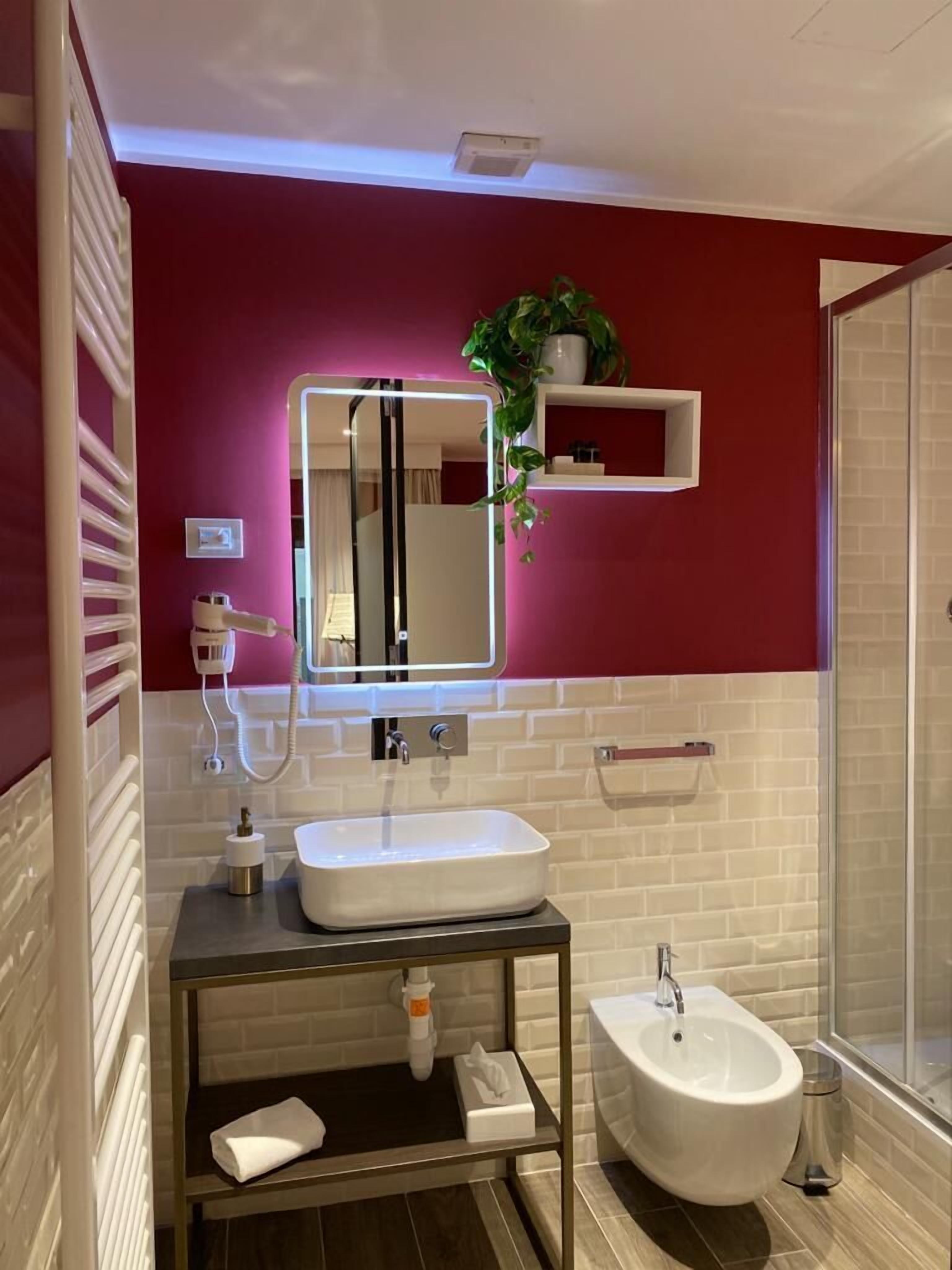 A modern bathroom with a white sink, a bidet, a mirror, and a potted plant on a shelf.
