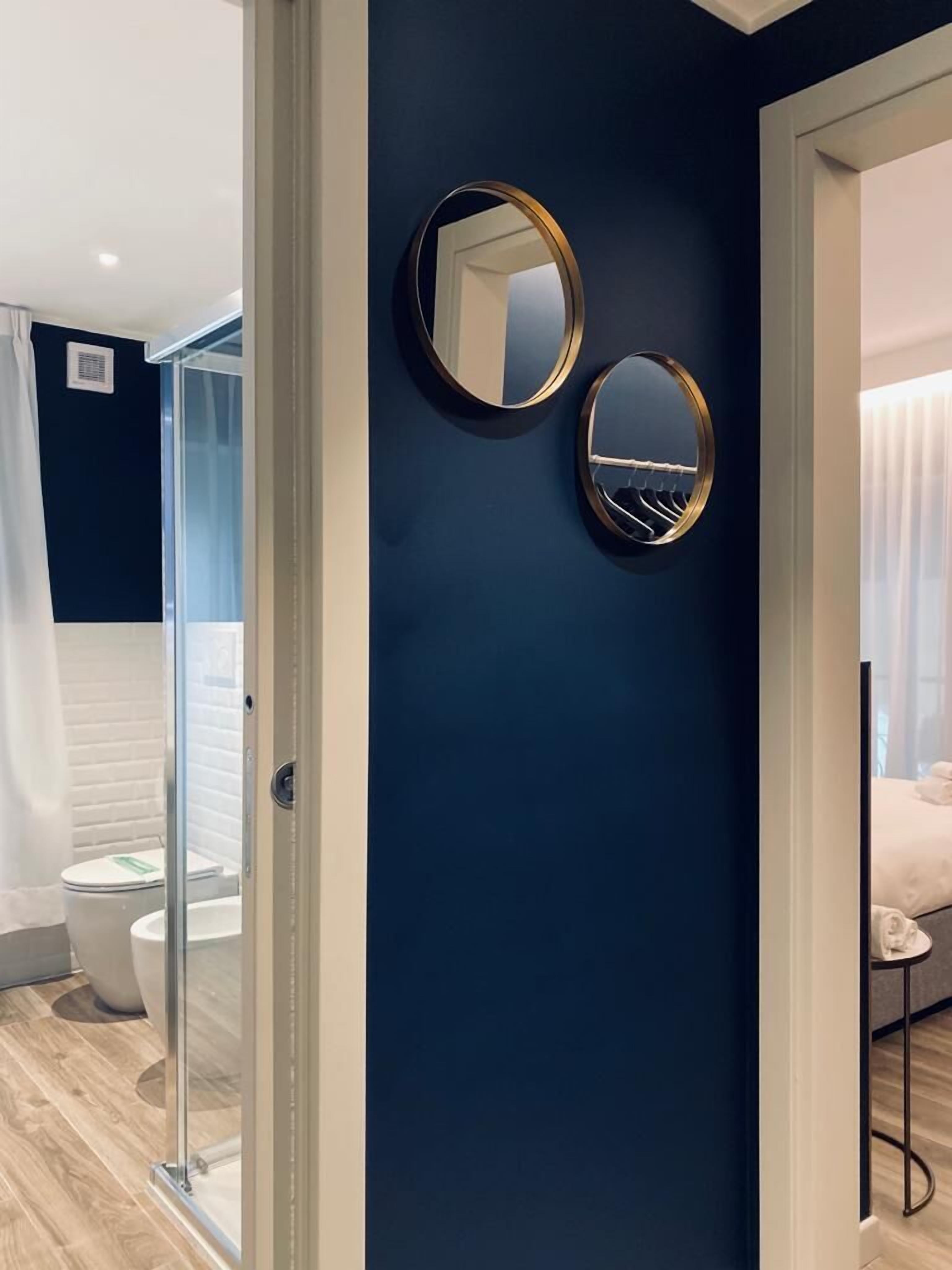 A modern bathroom with a glass shower enclosure, a white toilet, and a dark blue wall with two round mirrors.