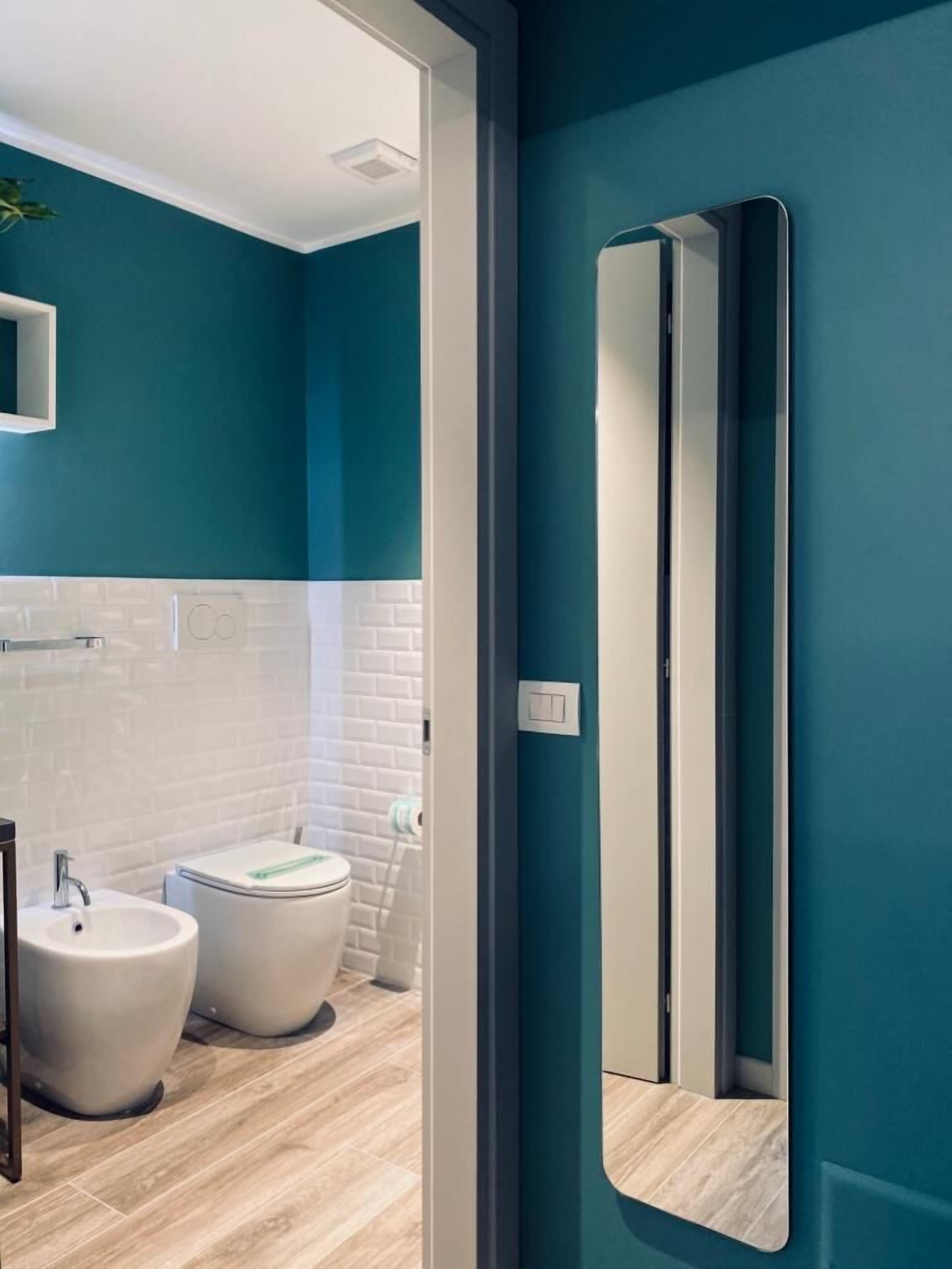 Ein modernes Badezimmer mit türkisfarbenen Wänden, weißen Ziegelfliesen, einem weißen Waschbecken und zwei Toiletten.