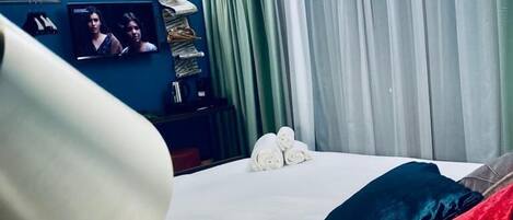 Una habitación de hotel con cama, televisión y ventana con cortinas.