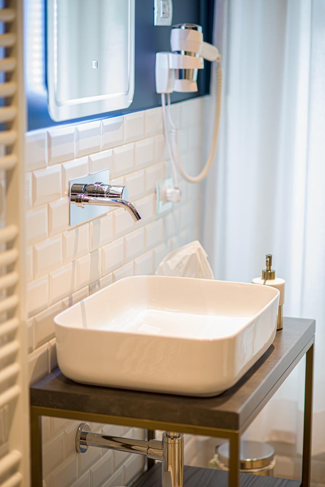 Ein Badezimmer mit einem weißen Waschbecken auf einer dunklen Arbeitsplatte, einem chromfarbenen Wasserhahn und einer Wandbrause.