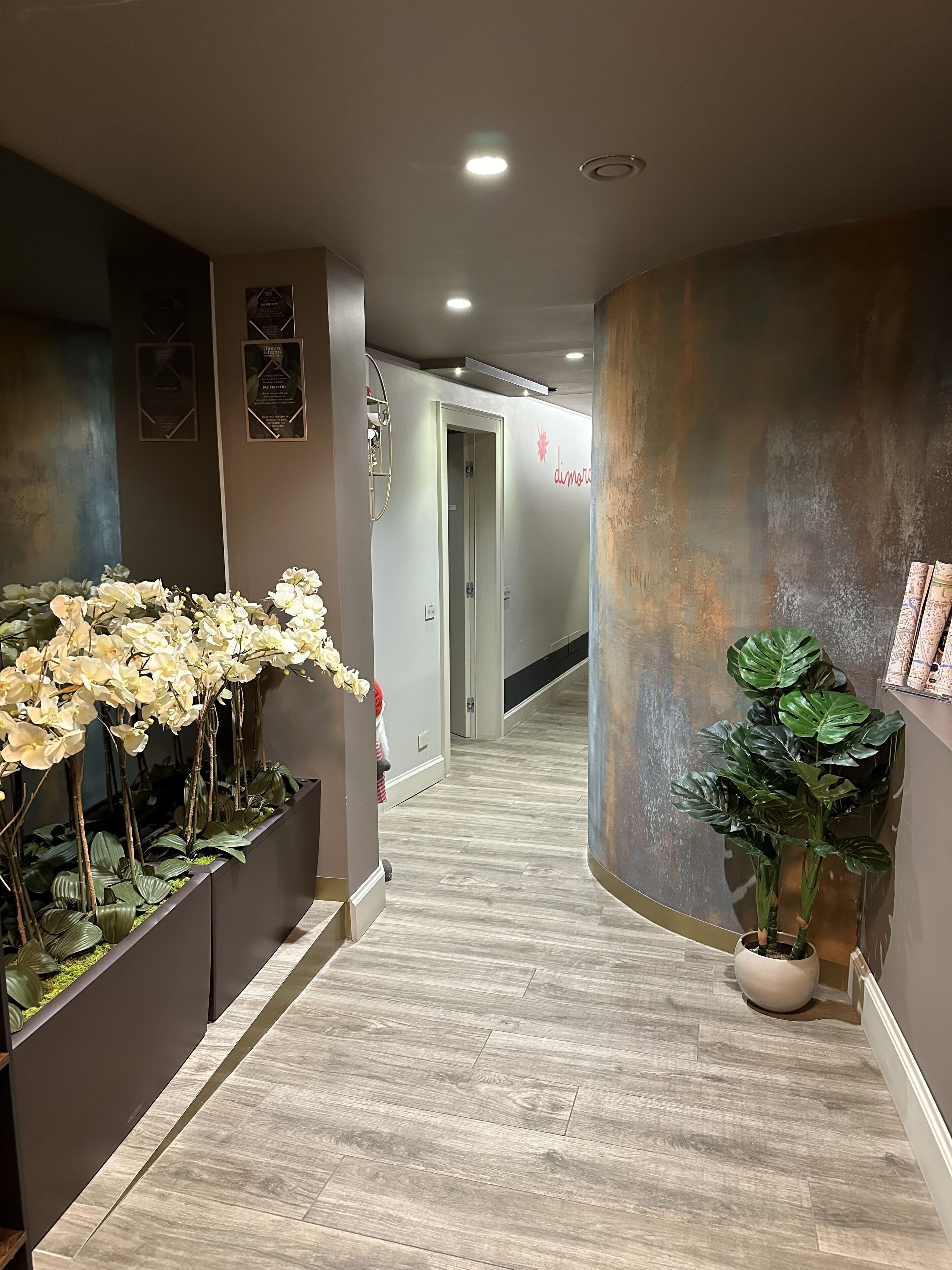 A hallway with a wooden floor, a potted plant, and a wall with a logo.