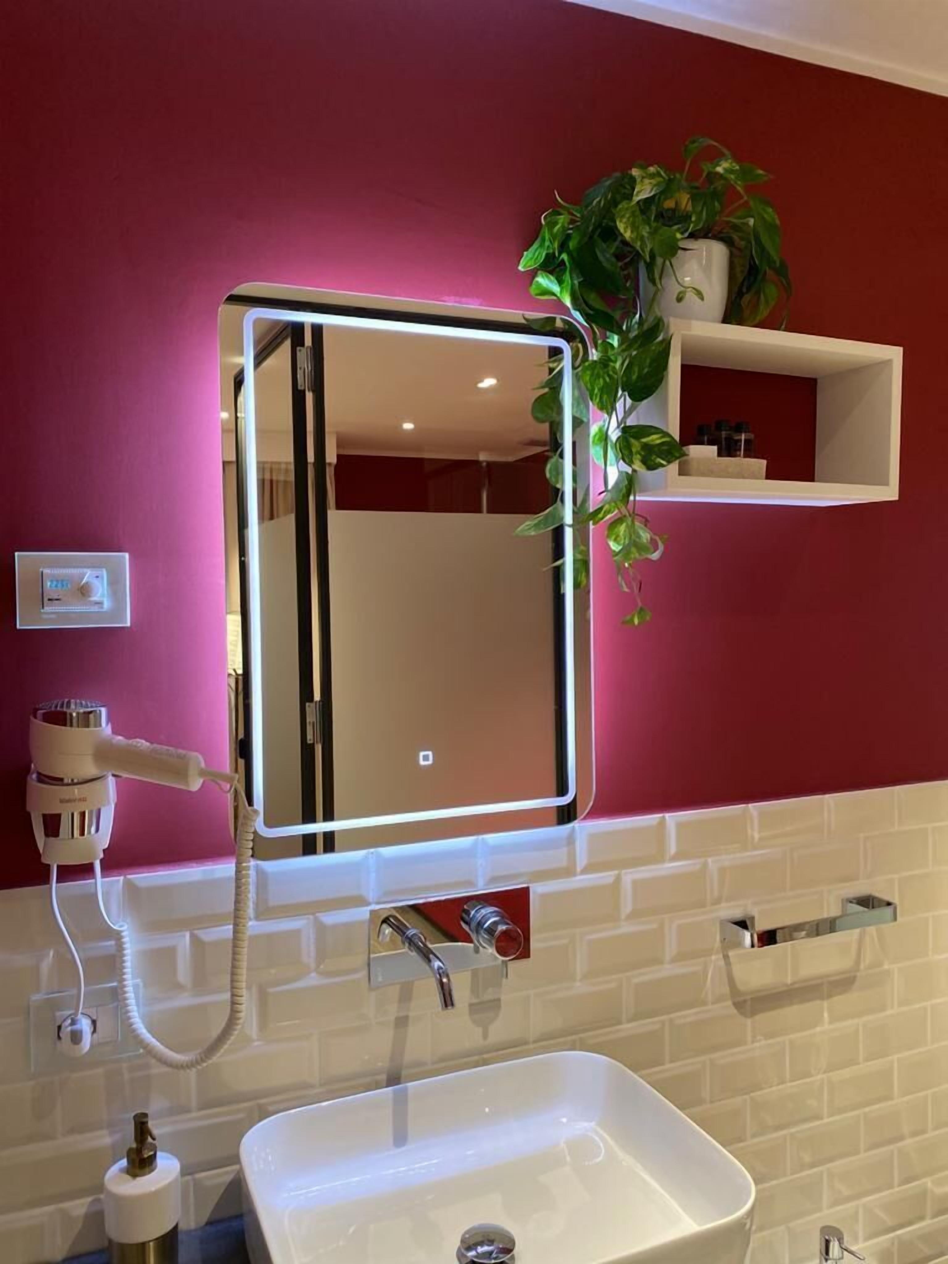 A bathroom with a white sink, a mirror with LED lights, a hairdryer, and a potted plant on a shelf.