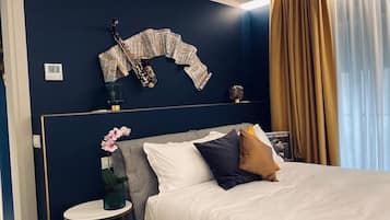 Et pænt indrettet hotelværelse med en seng, et lille sengebord med en vase blomster, en saxofon på væggen og en bog med titlen "Ray Charles".