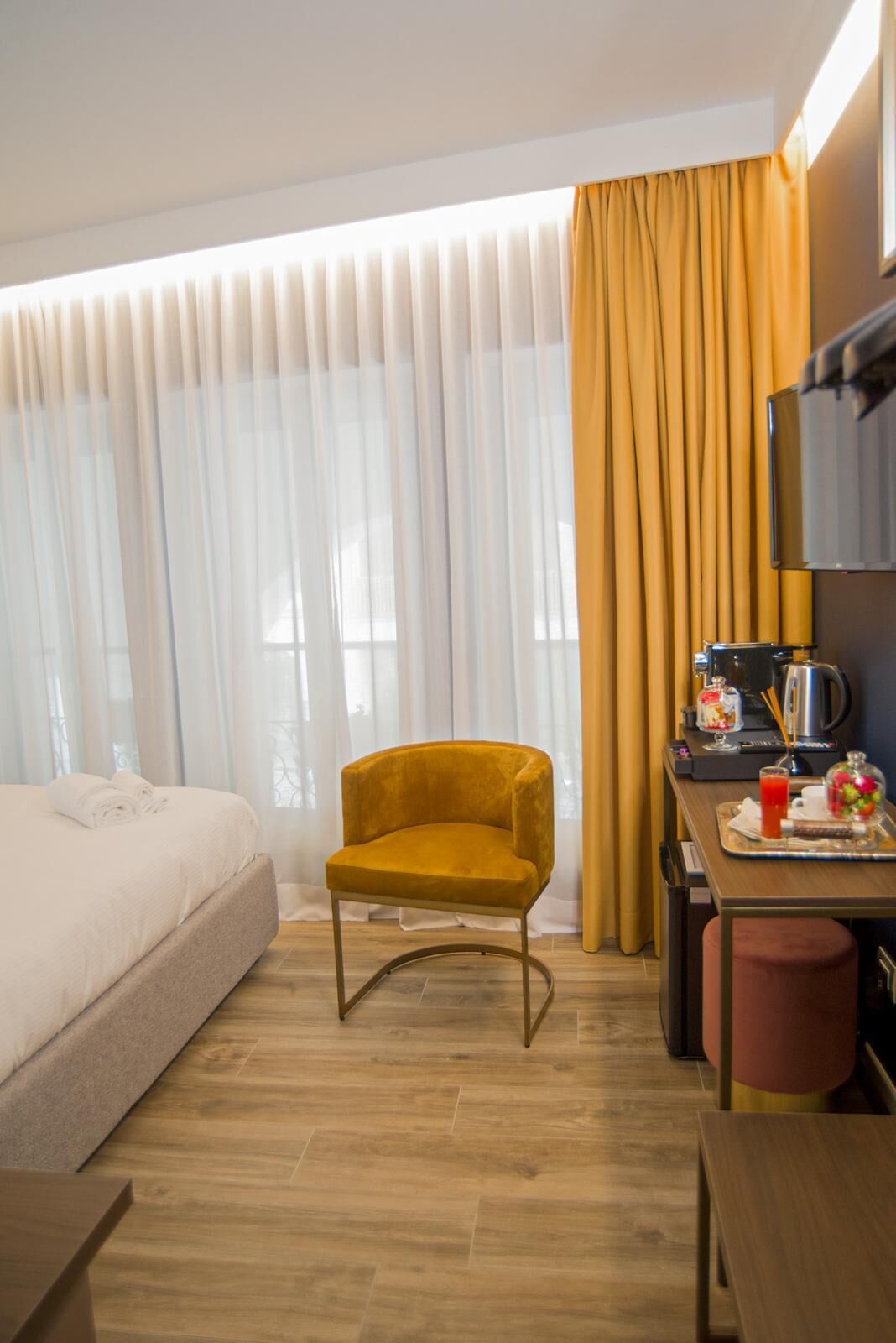 A hotel room with a bed, a yellow armchair, a dining table with a coffee machine, and a TV.