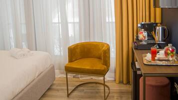 A hotel room with a bed, a yellow armchair, a dining table with a coffee machine, and a TV.