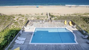 A wooden deck with a pool, beach chairs, and a view of the ocean. - OCEANFRONT, Community Pool and beach walkway! KD220, Feelin Nauti (Kill Devil Hills)