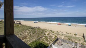 A beach view with a wooden deck, beach umbrellas, and a boardwalk leading to the shore. - OCEANFRONT, Community Pool and beach walkway! KD220, Feelin Nauti (Kill Devil Hills)