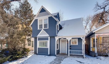 Charming two story blue home with crisp white trim, a snow covered yard, and a welcoming covered entry.

