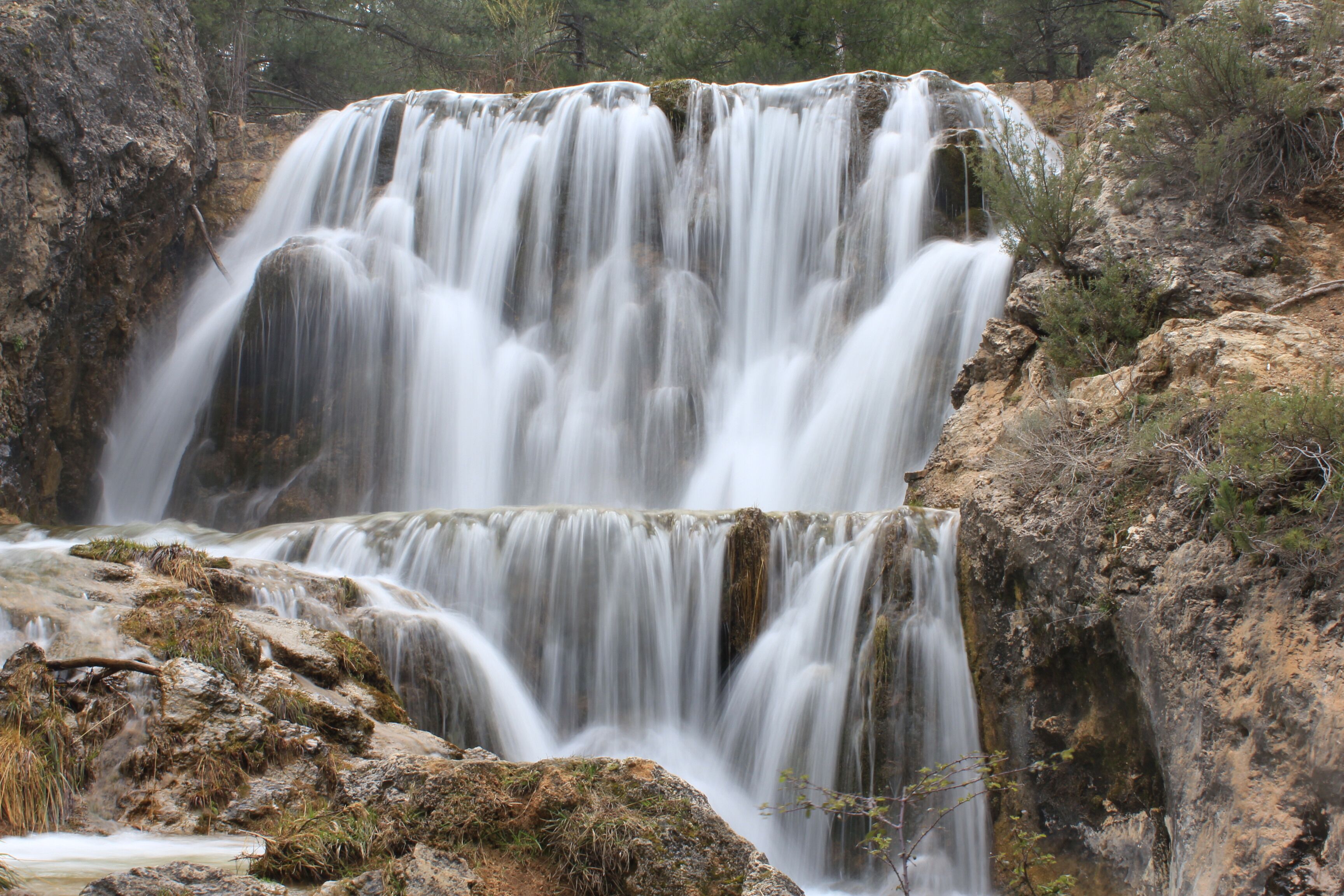 Una cascada se precipita sobre terreno rocoso con vegetación escasa.