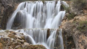 Una cascada se precipita sobre terreno rocoso con vegetación escasa.