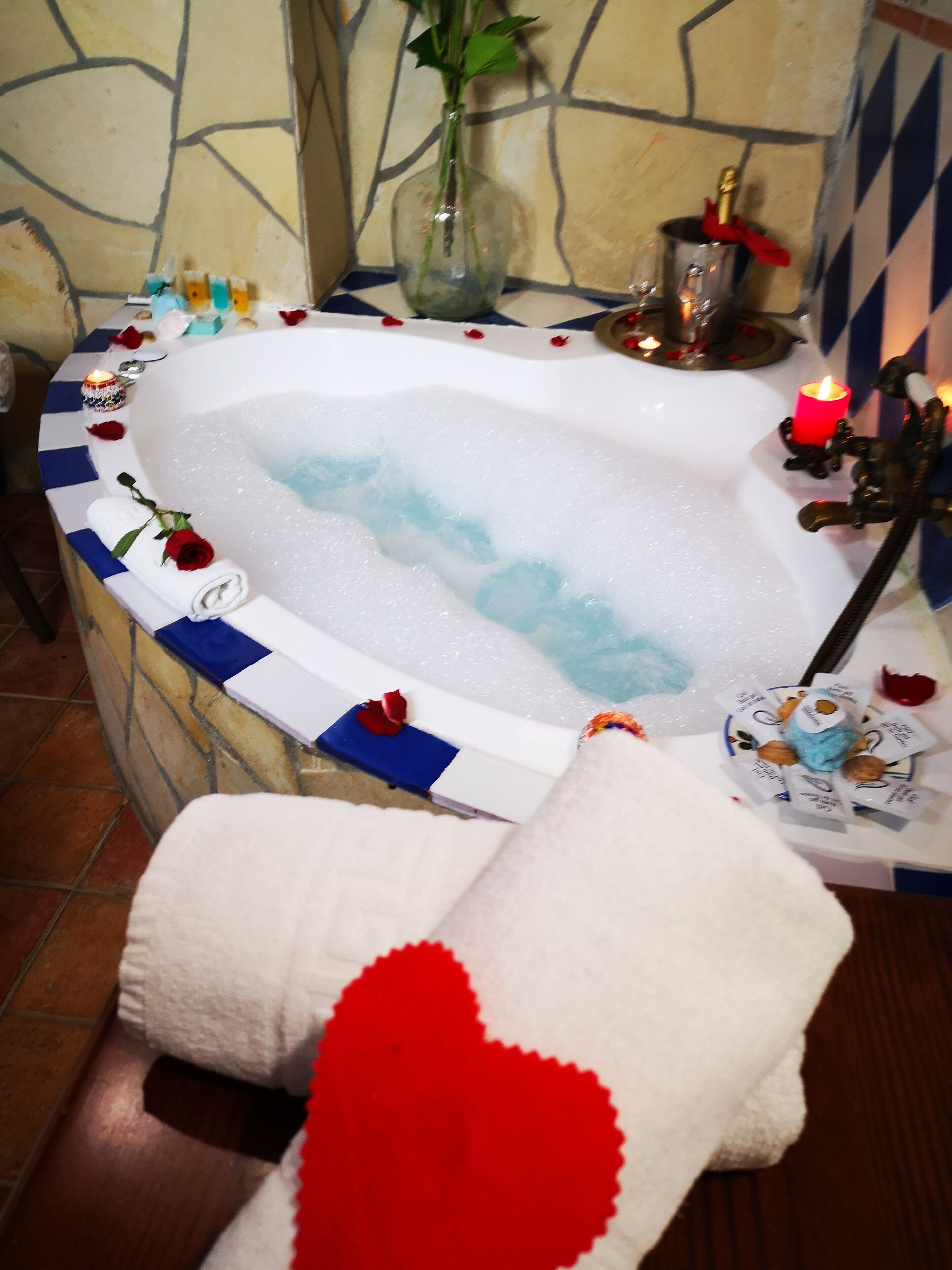 A bathtub with rose petals, candles, and a vase of flowers.