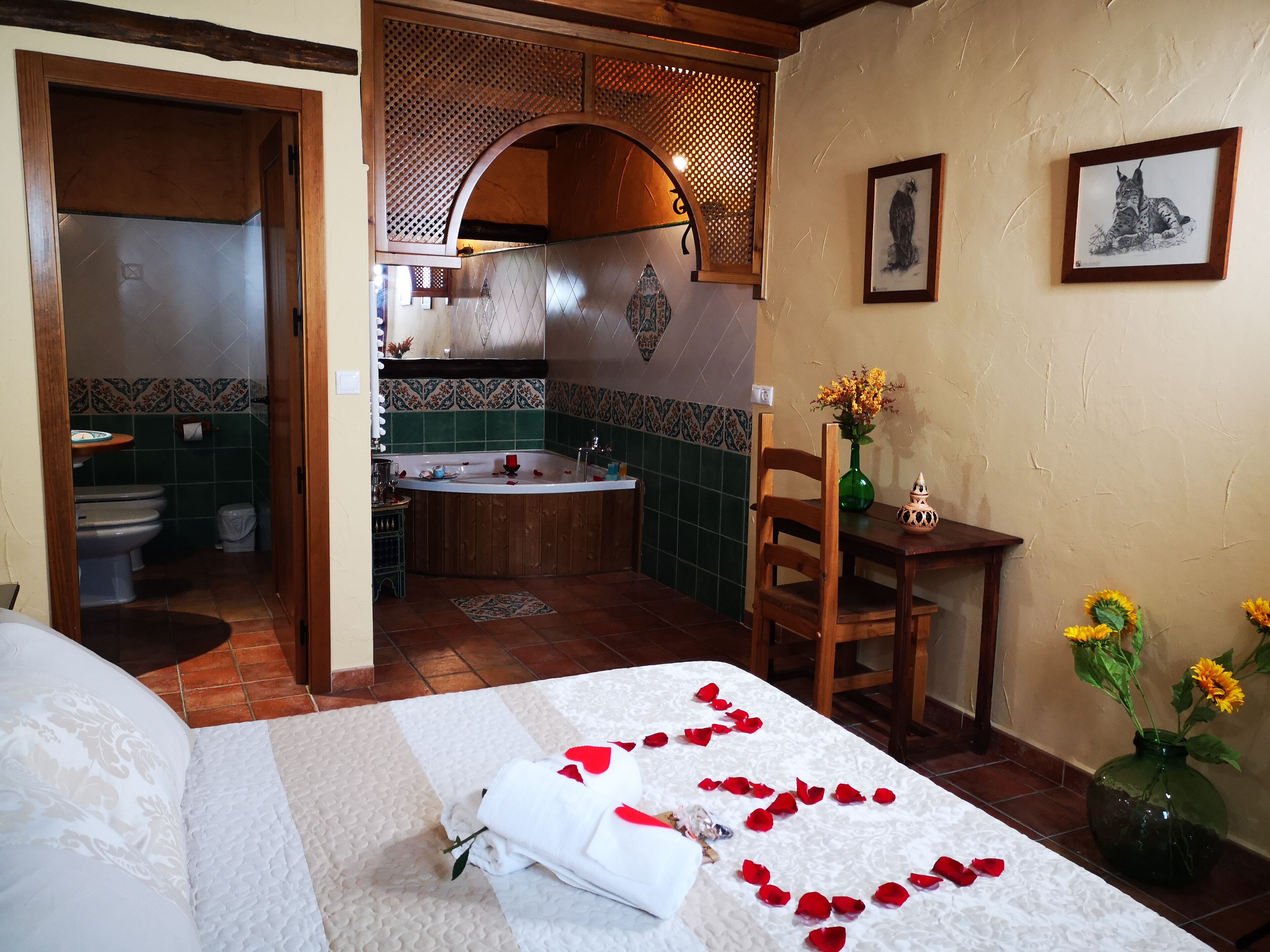 A hotel room with a bed, a bathroom, a wooden chair, and a table with a vase of flowers.