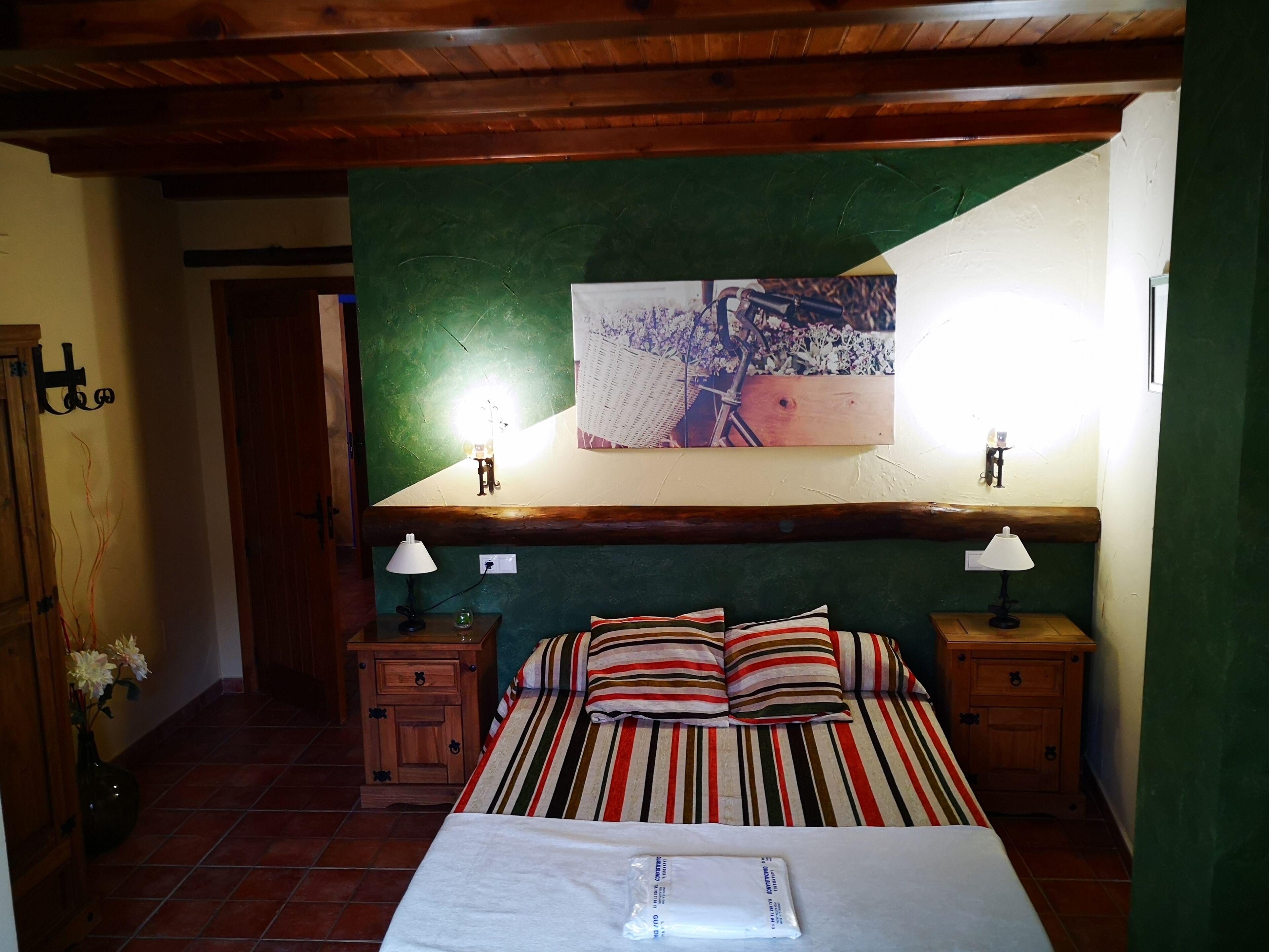 Camera da letto con un letto, due comodini, una testiera in legno, una parete verde decorativa e un quadro incorniciato sopra il letto.