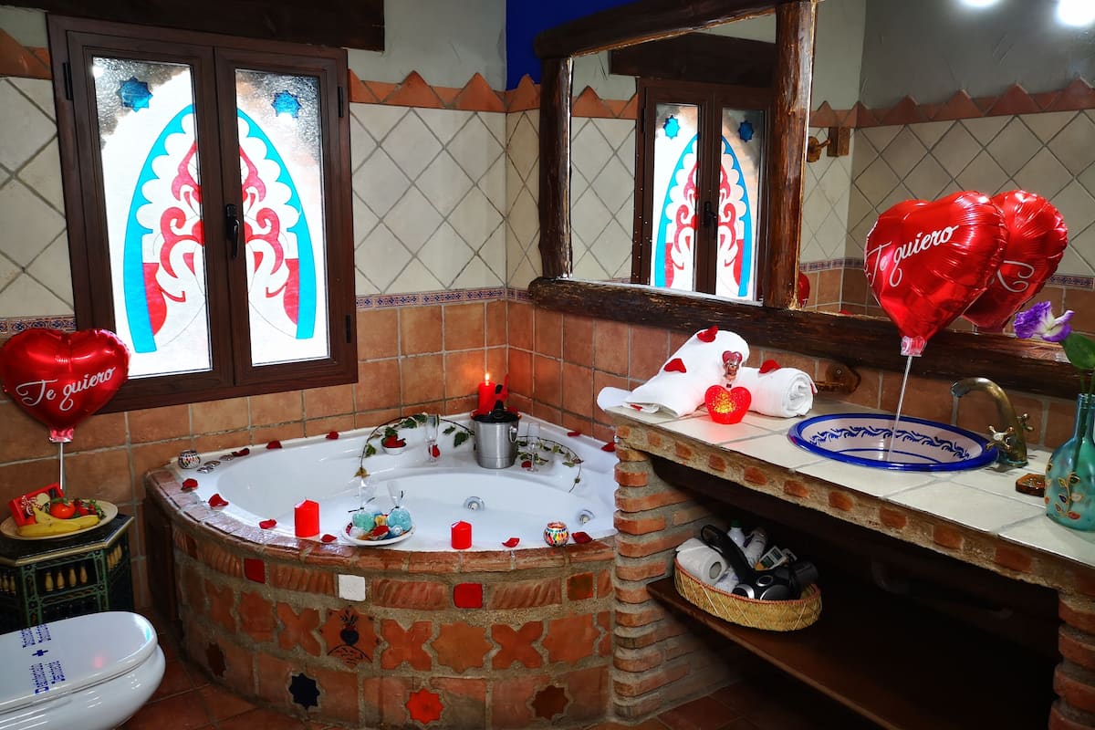 Ein Badezimmer mit einer Steinbadewanne, einem Spiegel, einem Waschbecken mit blauer Dekotasse und herzförmigen Ballons.