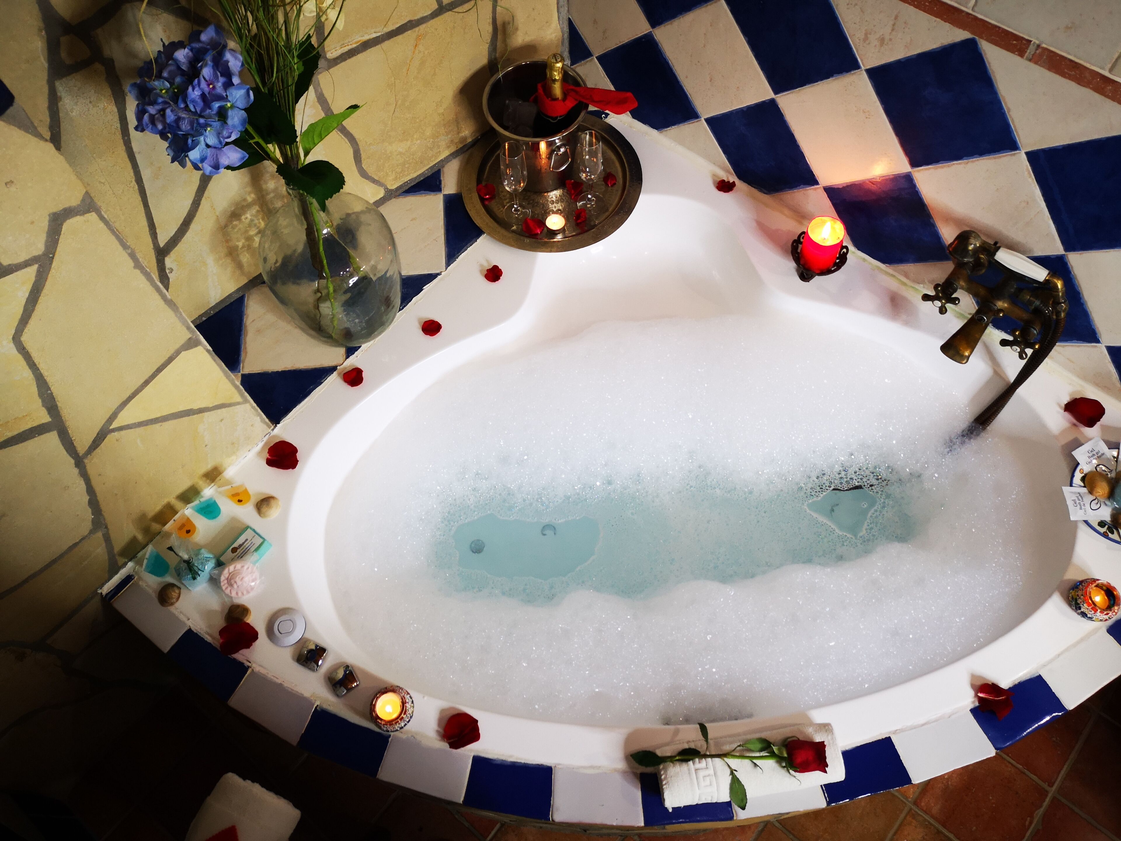 Une baignoire remplie de mousse, entourée d’objets décoratifs tels que des bougies, une rose et un vase de fleurs.