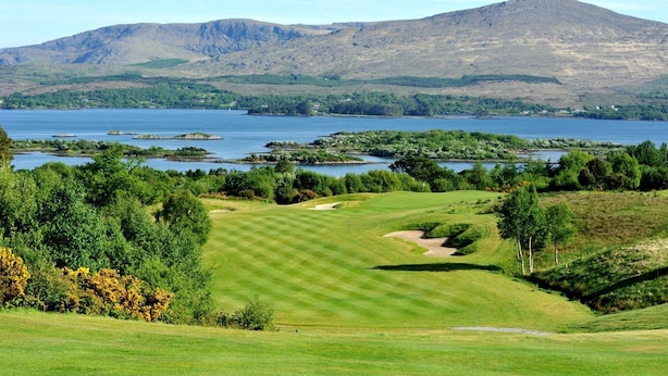 Un campo de golf con un lago y montañas al fondo.