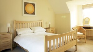Un dormitorio con una cama de madera, dos mesitas de noche, una silla, un escritorio y un espejo.