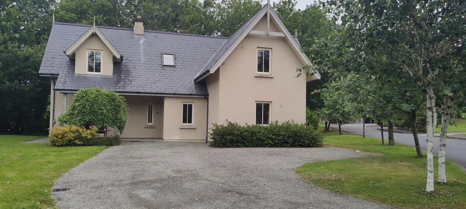A two-story house with a sloped roof, a front porch, and a gravel driveway.