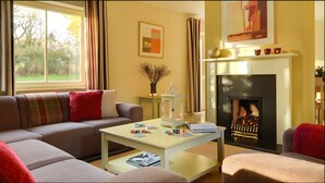 A cozy living room with a sofa, a coffee table with poker chips, a fireplace, and a painting on the wall. - Dunkerron Woods 4 Bedroom 4020 (Kenmare)