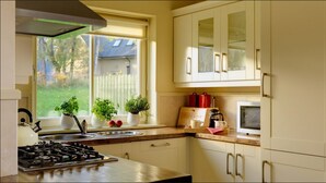 A kitchen with a gas stove, sink, and cabinets. There are potted plants on the windowsill, and a coffee maker on the counter. - Dunkerron Woods 4 Bedroom 4020 (Kenmare)