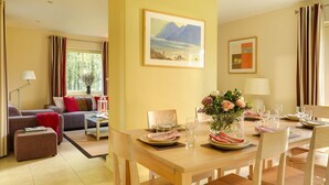 A well-lit room with a dining table set for four, a sofa, a lamp, and a painting on the wall. - Dunkerron Woods 4 Bedroom 4020 (Kenmare)