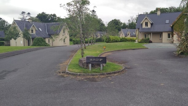 A residential area with houses, a driveway, and a sign indicating a property number. - Dunkerron Woods 3 Bedroom 4027 (Kenmare)