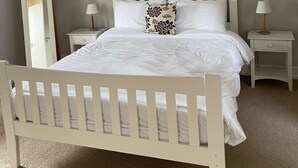 A bedroom with a white bed, two bedside tables with lamps, a mirror, and a colorful abstract painting on the wall. - Dunkerron Woods 3 Bedroom 4027 (Kenmare)