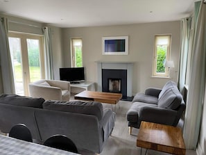 A modern living room with a fireplace, a flat-screen TV, and a sofa. - Dunkerron Woods 3 Bedroom 4027 (Kenmare)