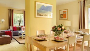Habitación de hotel con comedor, sofá, mesa preparada para dos personas y un cuadro en la pared.