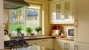 Una cocina con estufa a gas, lavamanos y ventana que da a un jardín trasero. Hay plantas en macetas en el alféizar y un microondas en la encimera.