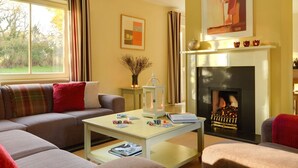 Una sala de estar acogedora con un sofá, una mesa de centro con cartas, una chimenea y una ventana con cortinas.
