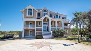 A large, multi-story house with a prominent front entrance, multiple balconies, and a driveway with a star-shaped design. - OCEANFRONT, Ocean views, Rec Rm, Private Pool, Hot Tub, PI52, Coco Palms (Corolla)