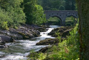 A river flowing under a stone bridge surrounded by lush greenery. - Dunkerron Woods 4 Bedroom 4009 (Kenmare)