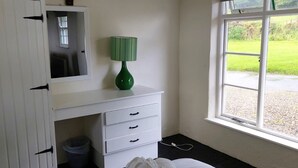 A hotel room with a bed, a white dresser with a mirror, a green lamp, and a window with a view of a grassy area. - Corofin Lake Cottage No 2 (Killinaboy)
