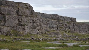 A rocky cliff with a grassy foreground and a cloudy sky. - Corofin Lake Cottage No 2 (Killinaboy)