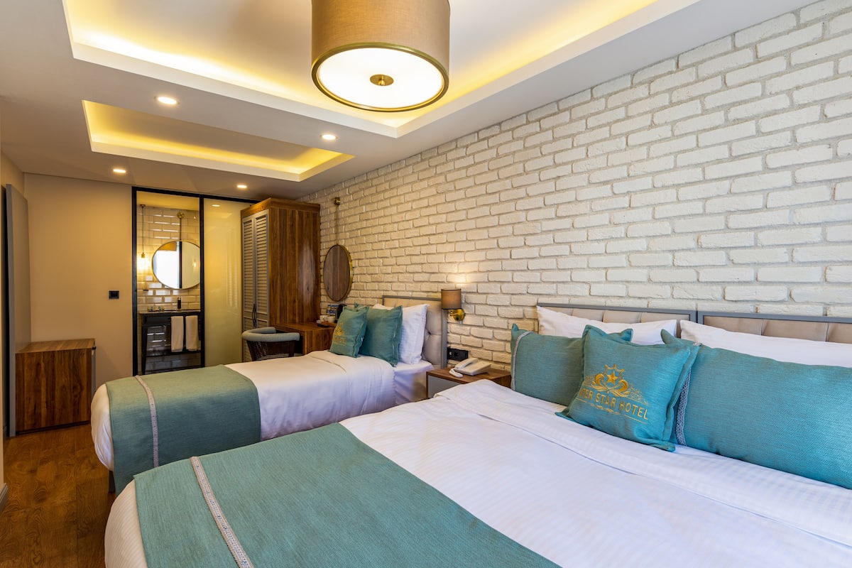 A hotel room with two beds, a brick wall, a wooden cabinet, and a nightstand with a lamp.