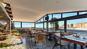 Un restaurant doté d’une terrasse donnant sur la mer, où l’on peut admirer une variété de plats exposés et où le sol est recouvert d’un motif décoratif.